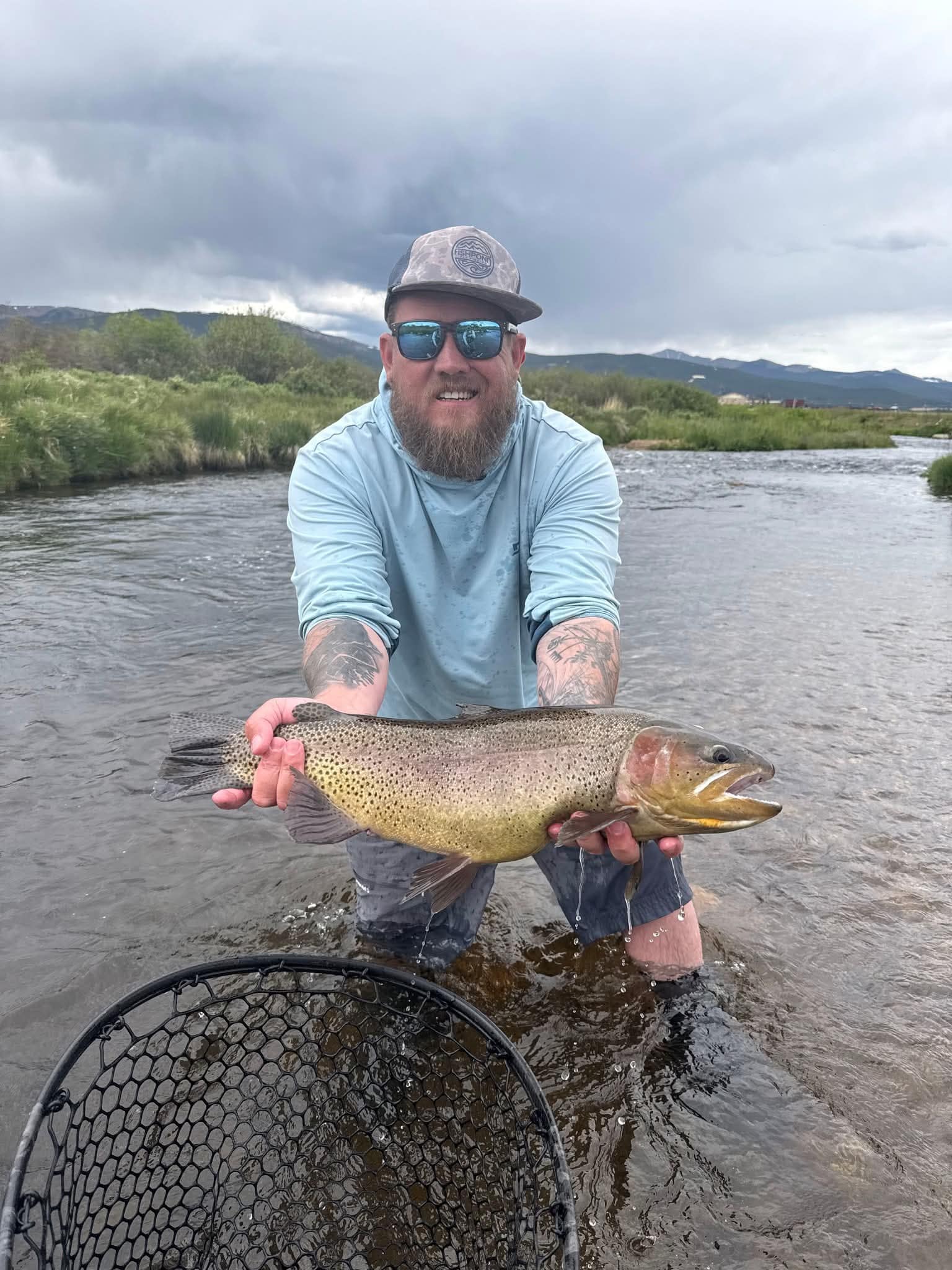 Cole Atchley holding a cutthroat trout on a Colorado river under a stormy sky