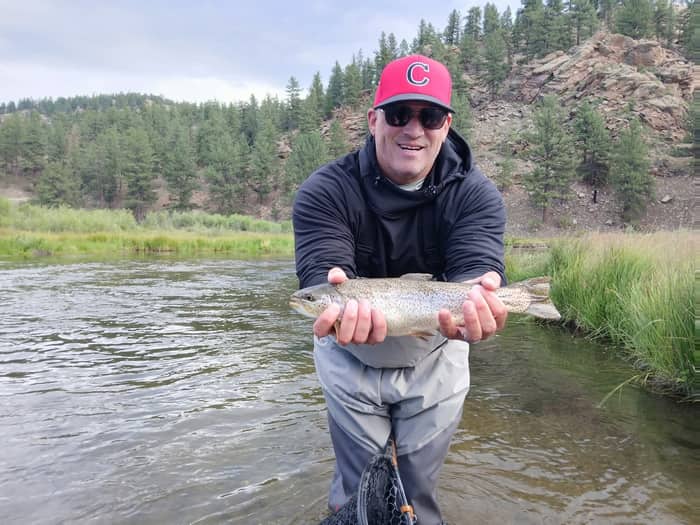 Angler holding a rainbow trout with pine-covered hills behind